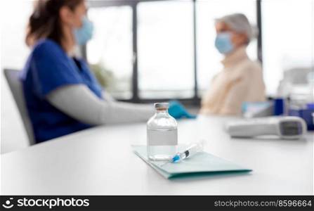 medicine, health and vaccination concept - bottle of medicine and syringe on table over doctor or nurse and patient at hospital. bottle of medicine or vaccine and syringe on table