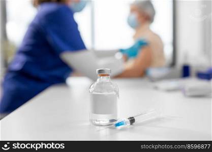 medicine, health and vaccination concept - bottle of medicine and syringe on table over doctor or nurse making vaccine or drug injection to patient at hospital. bottle of medicine or vaccine and syringe on table