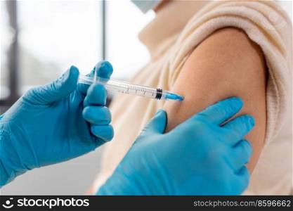 medicine, health and vaccination concept - close up of doctor or nurse with syringe making vaccine or drug injection to woman at hospital. nurse with syringe making injection to woman