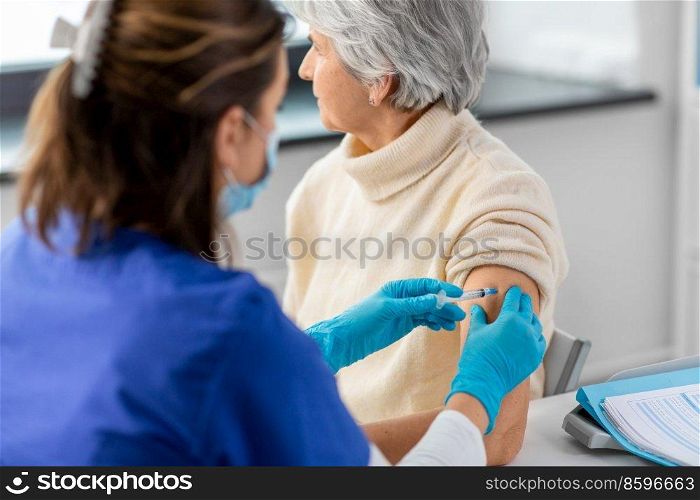 medicine, health and vaccination concept - close up of doctor or nurse with syringe making vaccine or drug injection to senior woman in mask at hospital. nurse with syringe making injection to woman