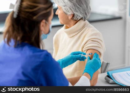 medicine, health and vaccination concept - close up of doctor or nurse with syringe making vaccine or drug injection to senior woman in mask at hospital. nurse with syringe making injection to woman