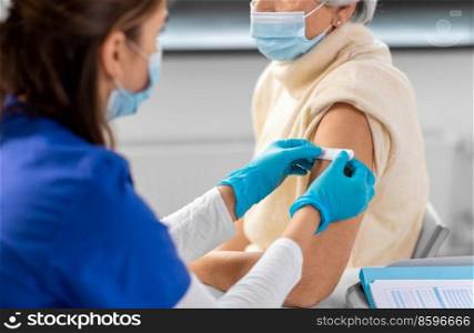 medicine, health and vaccination concept - close up of doctor or nurse applying medical patch to vaccinated senior woman in mask at hospital. nurse applying medical patch to vaccinated woman