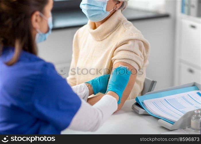 medicine, health and vaccination concept - close up of doctor or nurse with disinfecting arm skin of senior woman in mask at hospital. doctor preparing senior woman for vaccination