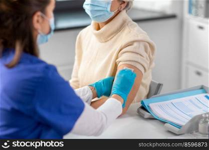 medicine, health and vaccination concept - close up of doctor or nurse with disinfecting arm skin of senior woman in mask at hospital. doctor preparing senior woman for vaccination