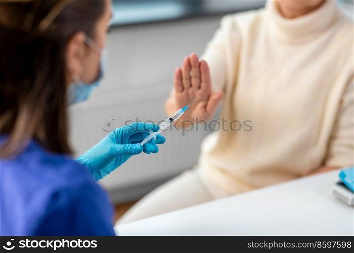medicine, health and vaccination concept - close up of doctor or nurse with syringe and senior woman refusing from vaccine or drug at hospital. nurse with syringe and woman refusing from vaccine