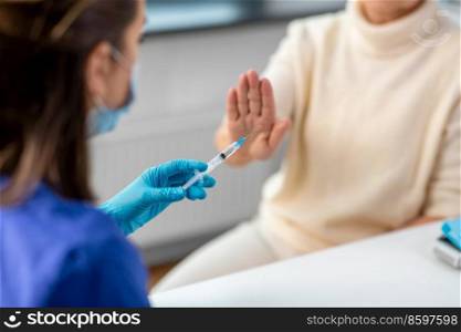 medicine, health and vaccination concept - close up of doctor or nurse with syringe and senior woman refusing from vaccine or drug at hospital. nurse with syringe and woman refusing from vaccine