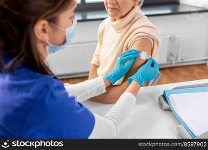 medicine, health and vaccination concept - close up of doctor or nurse applying medical patch to vaccinated senior woman in mask at hospital. nurse applying medical patch to vaccinated woman