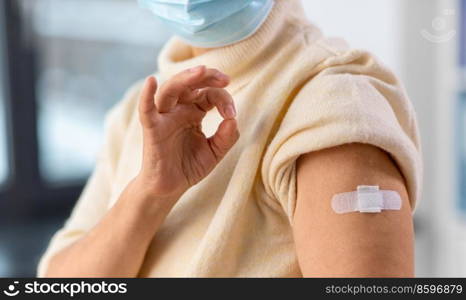 medicine, health and vaccination concept - close up of vaccinated senior woman with medical patch on arm showing ok gesture at hospital. vaccinated senior woman with medical patch on arm