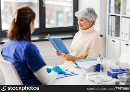 medicine, health and vaccination concept - doctor or nurse and senior woman reading medical brochure at hospital. doctor and senior woman reading medical brochure