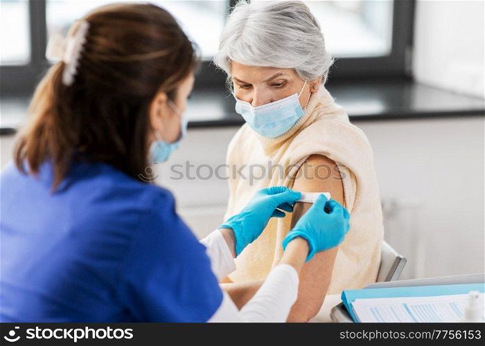 medicine, health and vaccination concept - doctor or nurse applying medical patch to vaccinated senior woman in mask at hospital. nurse applying medical patch to vaccinated woman
