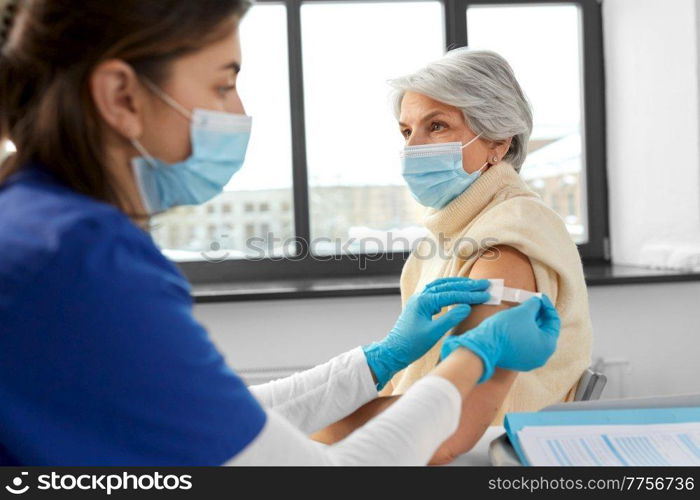 medicine, health and vaccination concept - doctor or nurse applying medical patch to vaccinated senior woman in mask at hospital. nurse applying medical patch to vaccinated woman