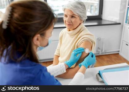medicine, health and vaccination concept - doctor or nurse applying medical patch to vaccinated senior woman at hospital. nurse applying medical patch to vaccinated woman