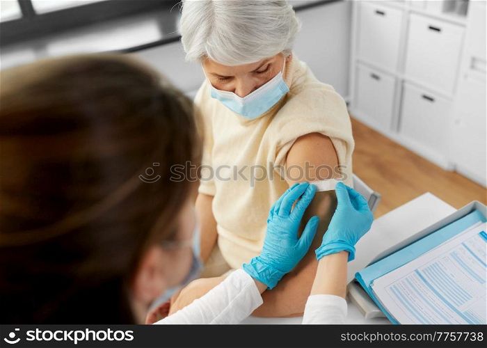 medicine, health and vaccination concept - doctor or nurse applying medical patch to vaccinated senior woman in mask at hospital. nurse applying medical patch to vaccinated woman
