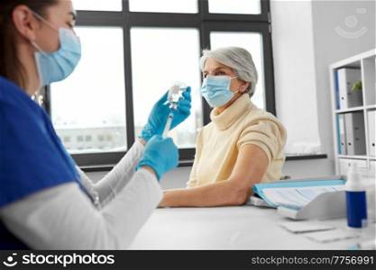 medicine, health and vaccination concept - doctor or nurse filling syringe with vaccine or drug and senior woman at hospital. doctor with syringe and senior woman at hospital