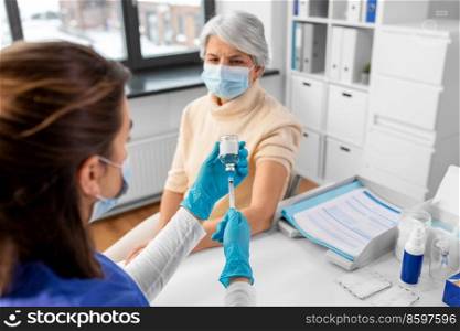 medicine, health and vaccination concept - doctor or nurse filling syringe with vaccine or drug and senior woman in mask at hospital. doctor with syringe and senior woman at hospital