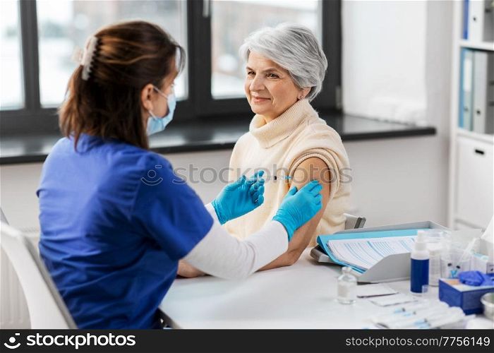 medicine, health and vaccination concept - doctor or nurse with syringe making vaccine or drug injection to senior woman at hospital. nurse with syringe making injection to woman
