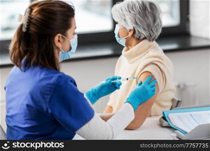medicine, health and vaccination concept - doctor or nurse with syringe making vaccine or drug injection to senior woman in mask at hospital. nurse with syringe making injection to woman