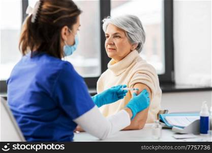 medicine, health and vaccination concept - doctor or nurse with syringe making vaccine or drug injection to senior woman at hospital. nurse with syringe making injection to woman