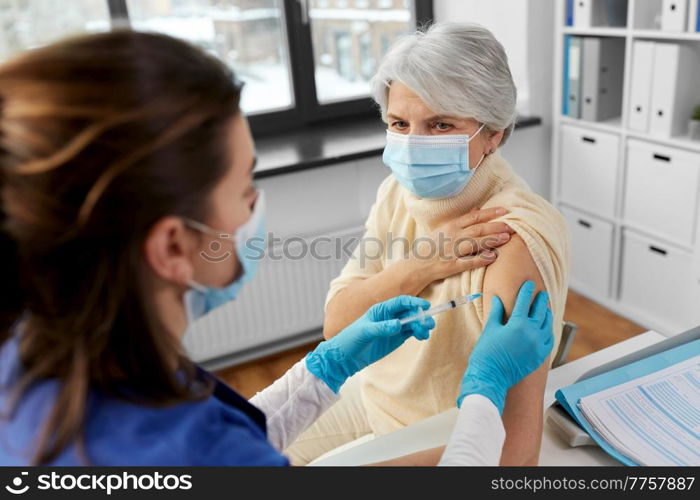 medicine, health and vaccination concept - doctor or nurse with syringe making vaccine or drug injection to senior woman in mask at hospital. nurse with syringe making injection to woman