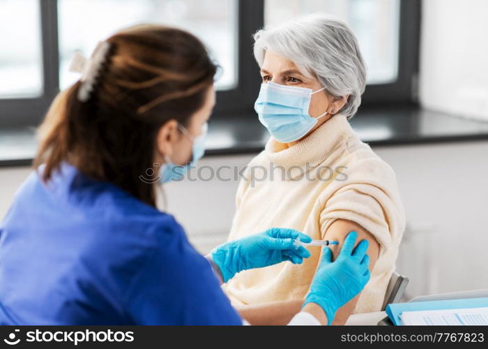 medicine, health and vaccination concept - doctor or nurse with syringe making vaccine or drug injection to senior woman in mask at hospital. nurse with syringe making injection to woman