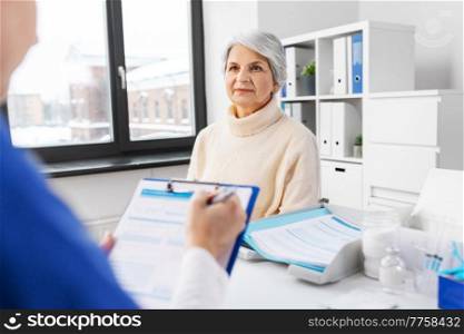 medicine, health and vaccination concept - doctor with clipboard and senior woman at hospital. doctor with clipboard and senior woman at hospital