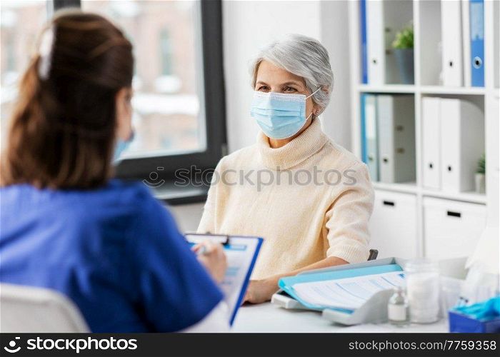 medicine, health and vaccination concept - doctor with clipboard and senior woman in mask at hospital. doctor with clipboard and senior woman at hospital