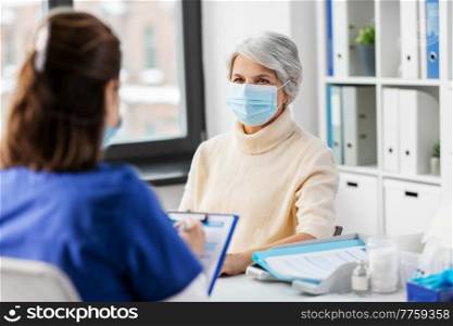 medicine, health and vaccination concept - doctor with clipboard and senior woman in mask at hospital. doctor with clipboard and senior woman at hospital