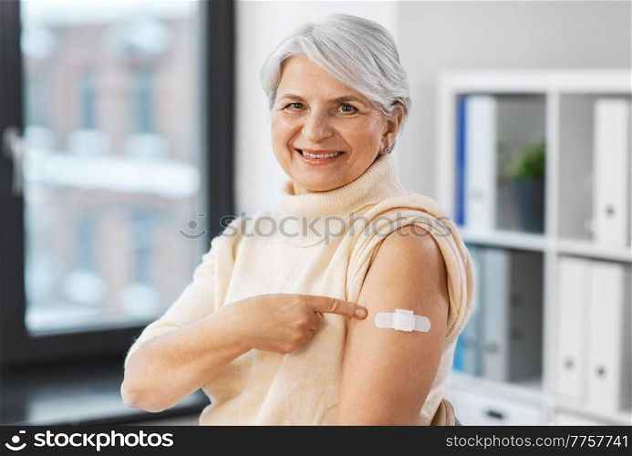 medicine, health and vaccination concept - happy smiling vaccinated senior woman showing medical patch on her arm at hospital. smiling vaccinated woman with medical patch on arm