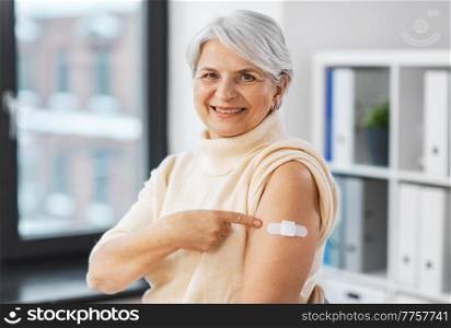 medicine, health and vaccination concept - happy smiling vaccinated senior woman showing medical patch on her arm at hospital. smiling vaccinated woman with medical patch on arm