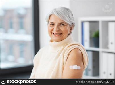 medicine, health and vaccination concept - happy smiling vaccinated senior woman with medical patch on arm at hospital. smiling vaccinated woman with medical patch on arm