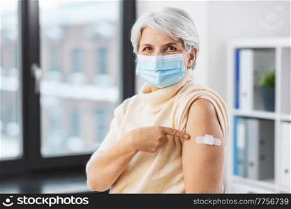medicine, health and vaccination concept - vaccinated senior woman in mask showing medical patch on her arm at hospital. vaccinated woman in mask with medical patch on arm