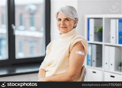 medicine, health and vaccination concept - vaccinated senior woman with medical patch on arm at hospital. vaccinated woman with medical patch on arm
