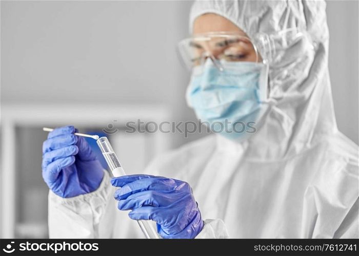 medicine, health and virus concept - close up of young female doctor or scientist in face protective medical mask, goggles and gloves holding beaker with coronavirus test and cotton swab. scientist holding beaker with coronavirus test