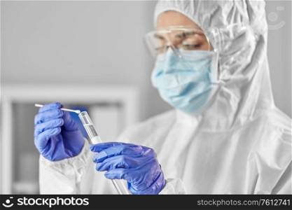 medicine, health and virus concept - close up of young female doctor or scientist in face protective medical mask, goggles and gloves holding beaker with coronavirus test and cotton swab. scientist holding beaker with coronavirus test