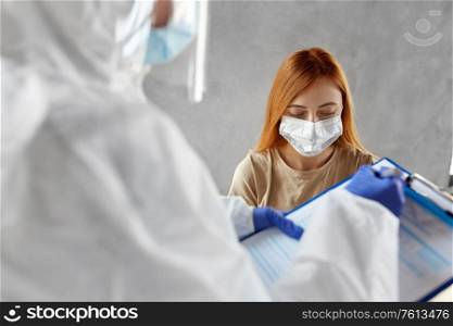 medicine, health and virus concept - patient in mask and doctor or healthcare worker in protective wear writing medical report on clipboard and doing coronavirus test. patient being tested for coronavirus disease