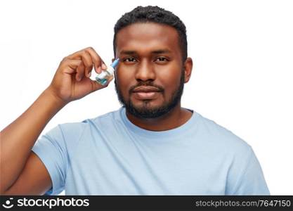 medicine, health and vision people concept - young african american man using eye drops over white background. young african american man using eye drops
