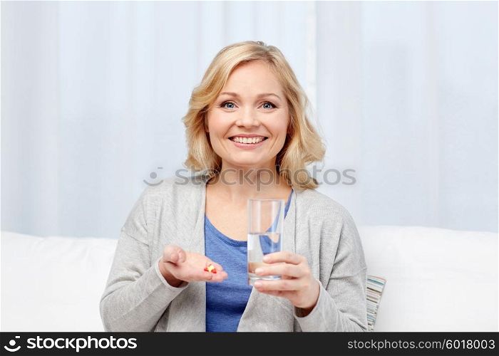 medicine, health care and people concept - happy middle aged woman with medicine and water glass at home