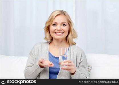 medicine, health care and people concept - happy middle aged woman with medicine and water glass at home