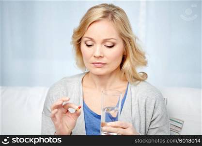 medicine, health care and people concept - middle aged woman with medicine and water glass at home