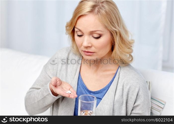 medicine, health care and people concept - middle aged woman with medicine and water glass at home
