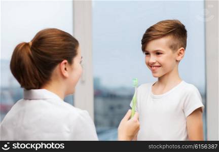 medicine, health care, dentistry, hygiene and people concept - doctor or dentist with toothbrush and happy boy in clinic
