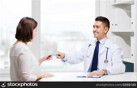 medicine, health care, medication and people concept - smiling doctor with clipboard giving pills to young woman at hospital