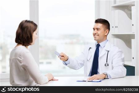 medicine, health care, medication and people concept - smiling doctor with clipboard giving pills to young woman at hospital