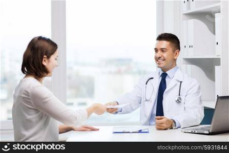 medicine, health care, meeting and people concept - smiling doctor with clipboard and laptop computer giving medical prescription or certificate to young woman at hospital