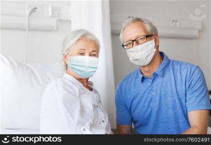 medicine, health safety and pandemic concept - happy senior man wearing face protective medical mask for protection from virus disease visiting his wife at hospital ward. senior couple in face masks meeting at hospital