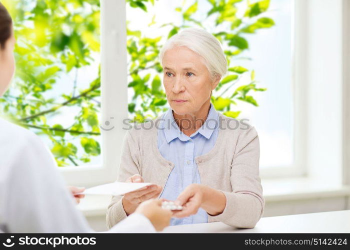 medicine, healthcare and age concept - doctor giving prescription and pills to senior woman at hospital over green natural background. doctor giving prescription and drug to woman