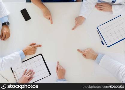 medicine, healthcare and cardiology concept - group of doctors with cardiograms, clipboards and laptop computer showing something imaginary on table. group of doctors with cardiograms working at table