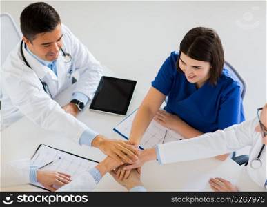 medicine, healthcare and cardiology concept - group of doctors with cardiograms, clipboards and tablet pc computer holding hands together at hospital. group of doctors holding hands together at table