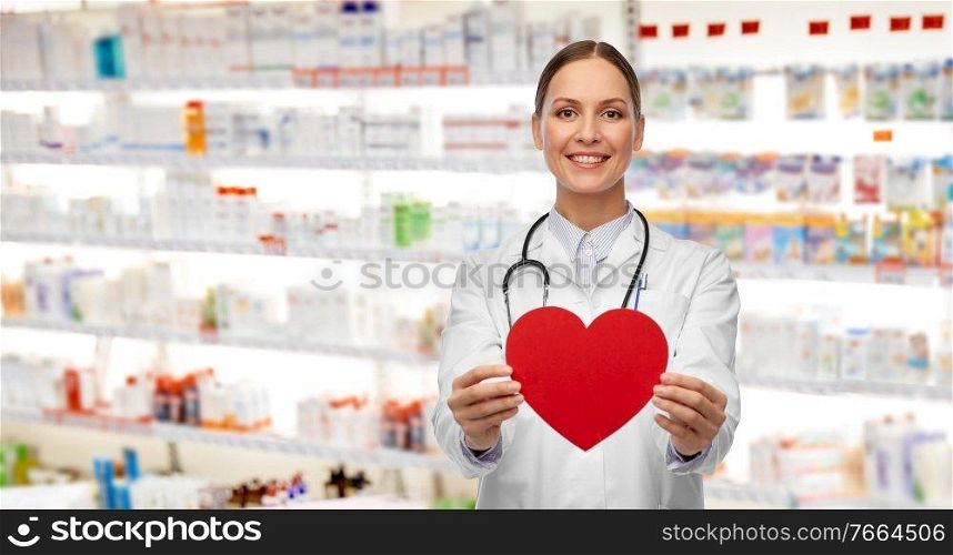 medicine, healthcare and cardiology concept - smiling female doctor with red heart and stethoscope over pharmacy background. smiling female doctor with heart and stethoscope