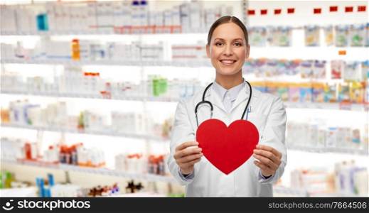 medicine, healthcare and cardiology concept - smiling female doctor with red heart and stethoscope over pharmacy background. smiling female doctor with heart and stethoscope